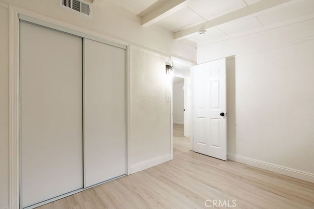 unfurnished bedroom with visible vents, baseboards, beamed ceiling, light wood-style flooring, and a closet