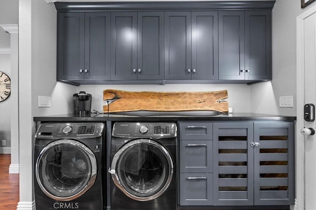 washroom featuring washing machine and clothes dryer, cabinet space, baseboards, and wood finished floors