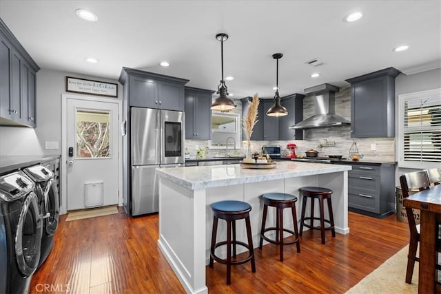 kitchen featuring washer and dryer, wall chimney exhaust hood, plenty of natural light, and stainless steel appliances