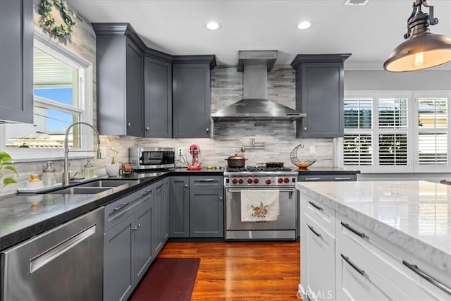 kitchen featuring light stone counters, a sink, stainless steel appliances, dark wood-type flooring, and wall chimney exhaust hood