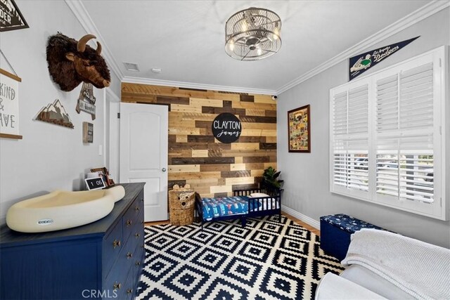 bedroom featuring an accent wall, visible vents, wood walls, and ornamental molding