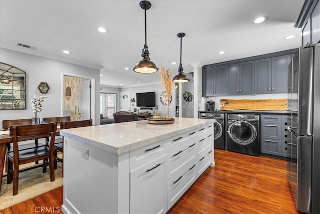 kitchen with light stone countertops, visible vents, washing machine and clothes dryer, dark wood-style flooring, and freestanding refrigerator