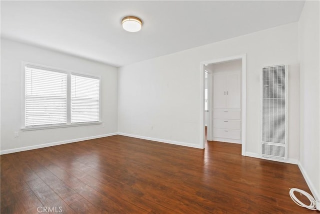 empty room featuring wood finished floors, a heating unit, and baseboards