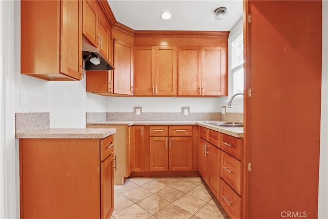 kitchen with under cabinet range hood, brown cabinets, light countertops, and a sink