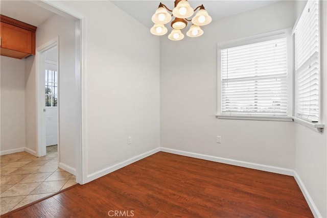 spare room featuring baseboards, light wood-type flooring, and an inviting chandelier