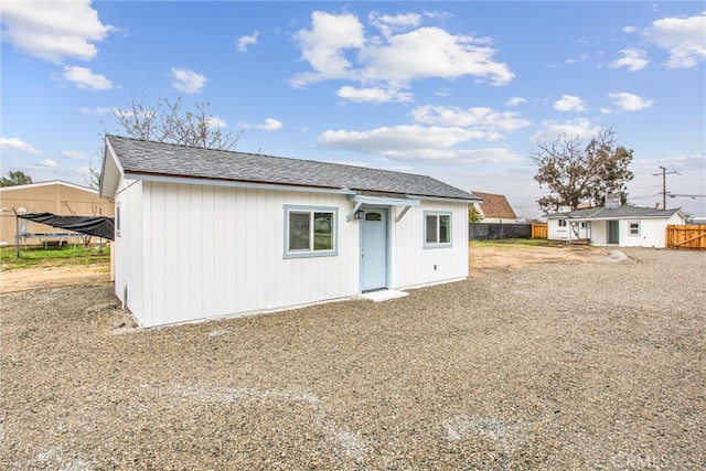 rear view of property featuring an outbuilding and fence