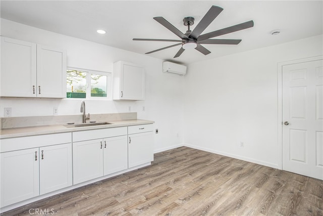 kitchen featuring a wall mounted air conditioner, light countertops, light wood-style flooring, white cabinets, and a sink