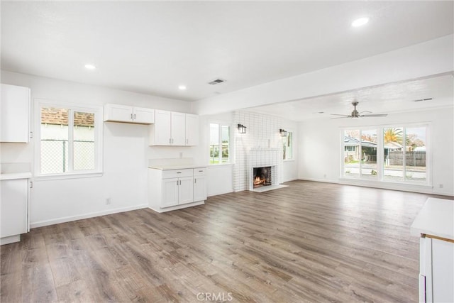 unfurnished living room featuring a brick fireplace, plenty of natural light, a ceiling fan, and light wood finished floors