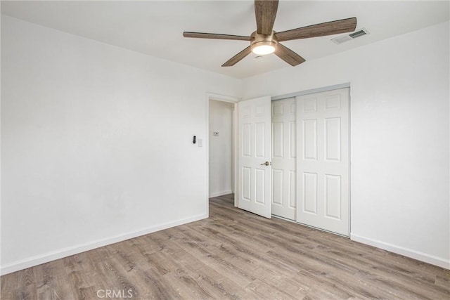 unfurnished bedroom with wood finished floors, baseboards, visible vents, ceiling fan, and a closet