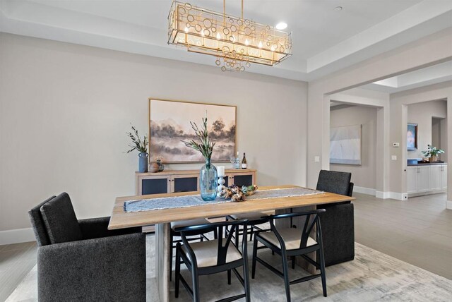 dining area with a notable chandelier, a tray ceiling, light wood-type flooring, and baseboards