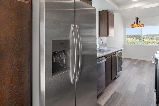 kitchen featuring dark brown cabinets, light countertops, light wood-style flooring, stainless steel appliances, and a sink