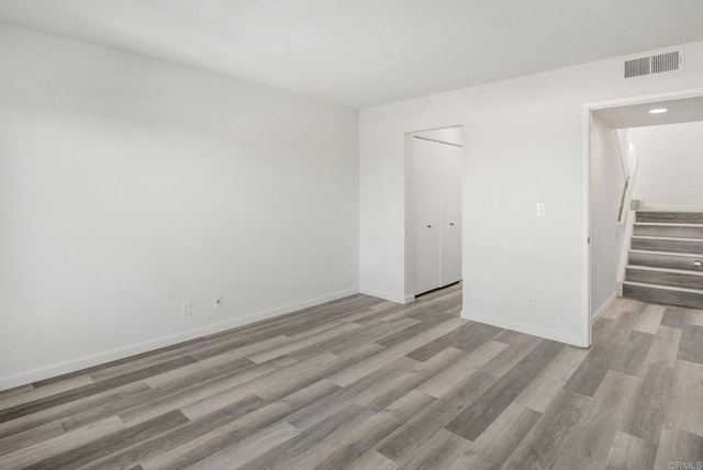 empty room featuring stairs, wood finished floors, visible vents, and baseboards