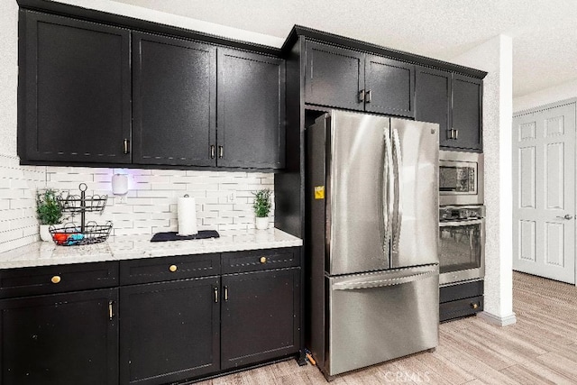 kitchen with stainless steel appliances, dark cabinets, light wood-type flooring, and backsplash