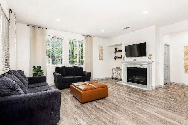 living room with light wood-style floors, a fireplace with raised hearth, recessed lighting, and baseboards