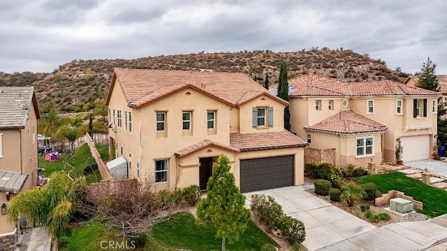 mediterranean / spanish-style house featuring an attached garage, concrete driveway, stucco siding, a tiled roof, and a mountain view