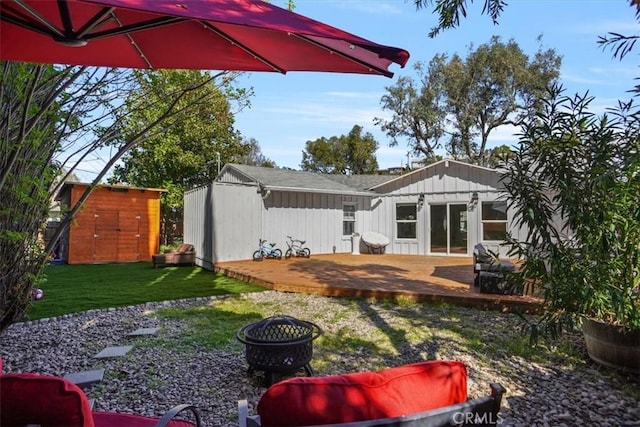 back of property with board and batten siding, a wooden deck, a lawn, an outdoor structure, and a storage unit