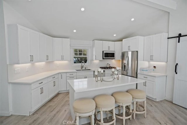 kitchen with a kitchen island, vaulted ceiling, a kitchen breakfast bar, stainless steel refrigerator with ice dispenser, and white cabinetry