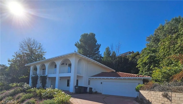 mediterranean / spanish-style home featuring stucco siding, a tile roof, concrete driveway, a garage, and a balcony