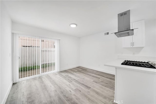 interior space with light wood-style flooring, black gas stovetop, white cabinetry, island range hood, and baseboards