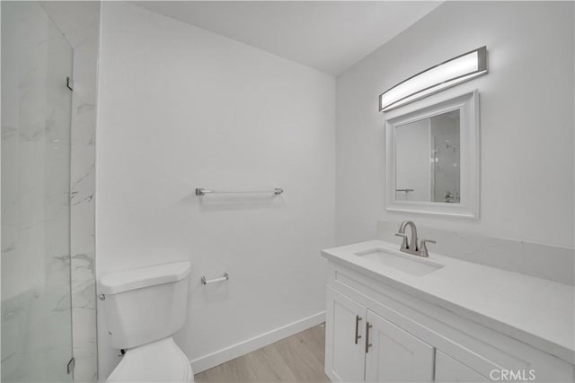 bathroom featuring a marble finish shower, baseboards, toilet, wood finished floors, and vanity