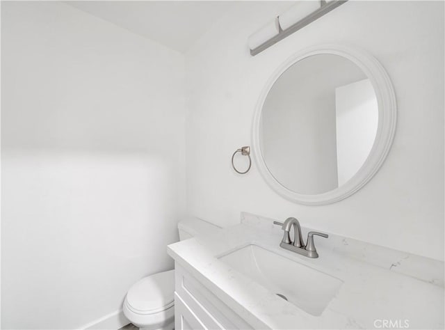 half bathroom featuring toilet, vanity, and baseboards