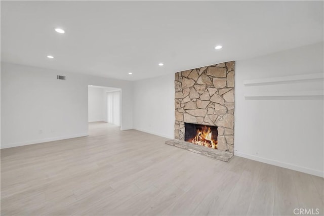 unfurnished living room with visible vents, light wood-style flooring, a stone fireplace, and baseboards