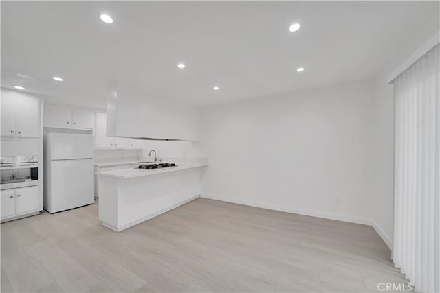 kitchen featuring oven, freestanding refrigerator, a peninsula, white cabinets, and light countertops