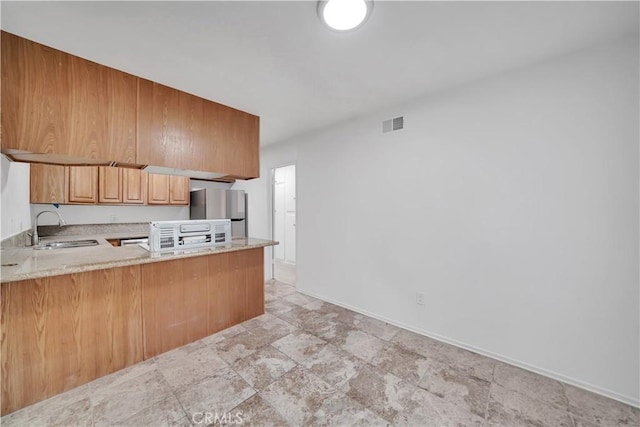 kitchen featuring visible vents, a sink, freestanding refrigerator, a peninsula, and baseboards