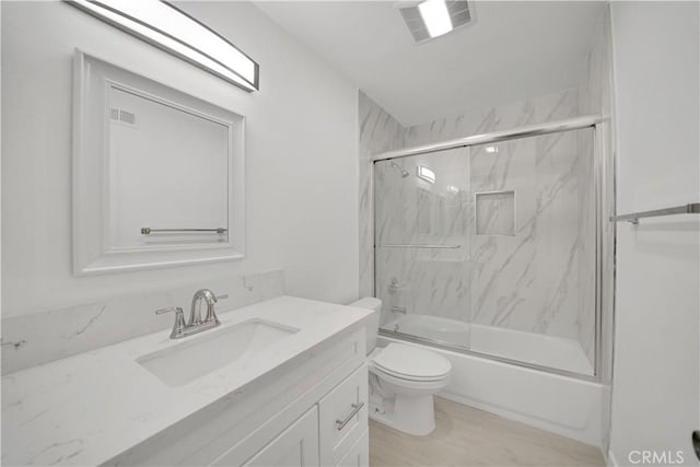 bathroom featuring visible vents, enclosed tub / shower combo, toilet, and vanity