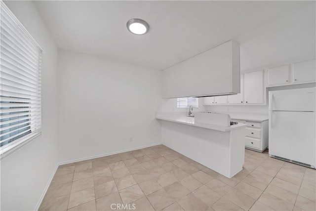 kitchen with baseboards, light countertops, a peninsula, freestanding refrigerator, and white cabinets