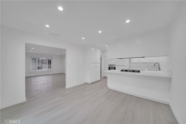 kitchen featuring a sink, open floor plan, recessed lighting, light wood-style floors, and white cabinets