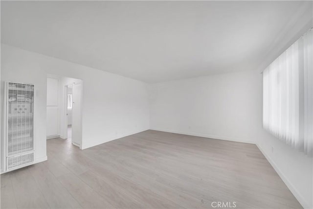 empty room featuring baseboards, a heating unit, and light wood-type flooring