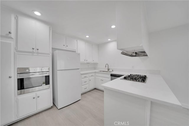 kitchen featuring a sink, appliances with stainless steel finishes, a peninsula, white cabinets, and light countertops