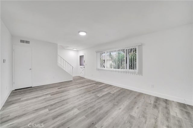 unfurnished room with visible vents, baseboards, wood finished floors, and stairs