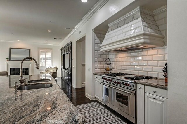 kitchen featuring a sink, crown molding, dark stone counters, range with two ovens, and custom exhaust hood