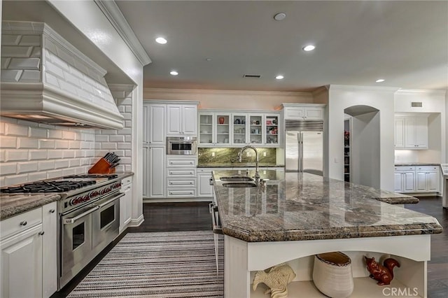 4 Andromeda Isle, Ladera Ranch, CA 92694 - kitchen with premium appliances, custom exhaust hood, white cabinetry, ornamental molding, and an island with sink