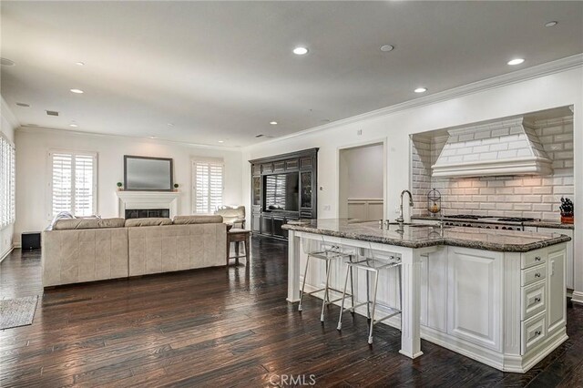 kitchen featuring ornamental molding, a sink, dark wood-type flooring, dark stone counters, and a kitchen bar