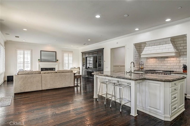 4 Andromeda Isle, Ladera Ranch, CA 92694 - kitchen featuring custom range hood, crown molding, dark wood-style flooring, a kitchen breakfast bar, and dark stone counters