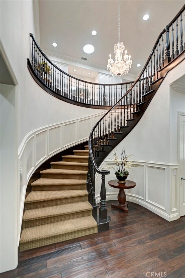 stairs featuring a towering ceiling, a notable chandelier, wood finished floors, and recessed lighting