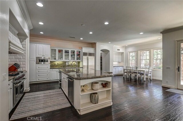 kitchen with arched walkways, a sink, open shelves, high quality appliances, and ornamental molding