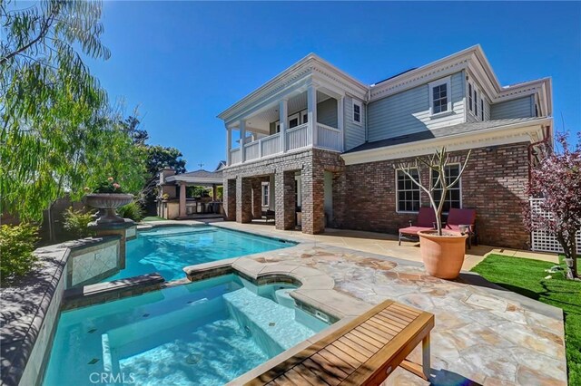 back of property featuring brick siding, a patio area, a balcony, and a pool with connected hot tub