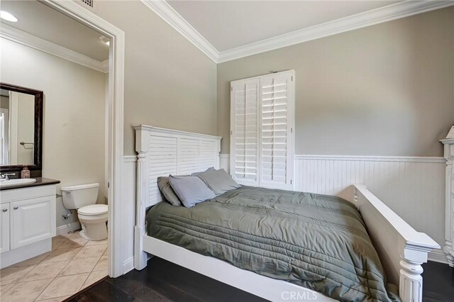 bedroom with ensuite bathroom, a wainscoted wall, ornamental molding, and a sink