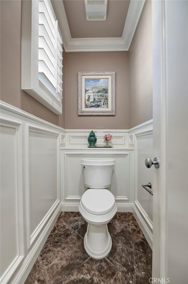 bathroom with wainscoting, toilet, marble finish floor, and a decorative wall