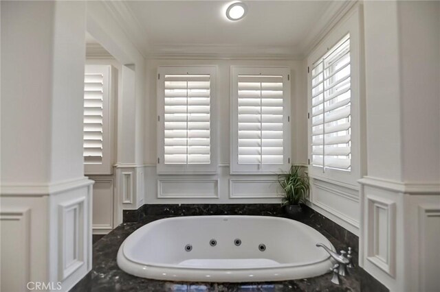 full bath featuring a whirlpool tub, a decorative wall, crown molding, and wainscoting