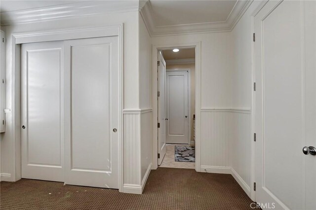 hallway featuring dark carpet, ornamental molding, and a decorative wall