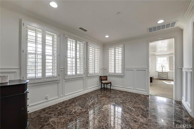 empty room with wainscoting, a decorative wall, ornamental molding, and visible vents