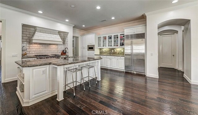 kitchen featuring a kitchen breakfast bar, dark wood finished floors, custom range hood, crown molding, and built in refrigerator