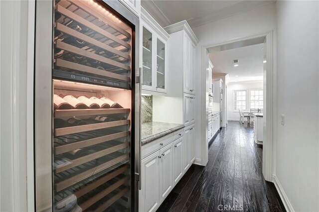 wine cellar with baseboards, beverage cooler, dark wood finished floors, and crown molding