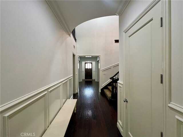 corridor featuring arched walkways, crown molding, a decorative wall, and dark wood-style floors