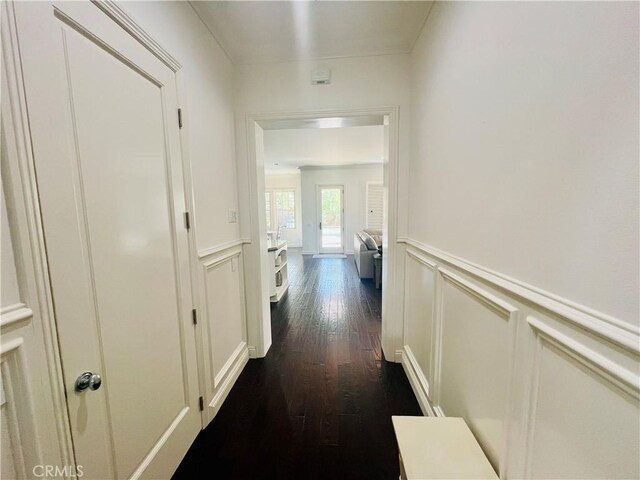 hall with dark wood finished floors, a decorative wall, and a wainscoted wall
